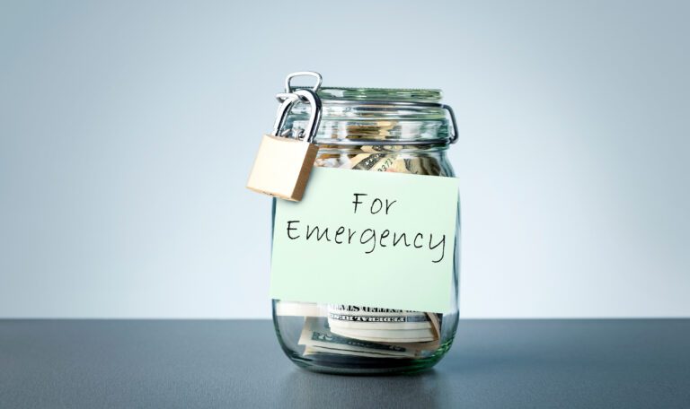 Money glass jar with written sticky note FOR EMERGENCY on gray background Concept of setting money saving goal for rainy day.